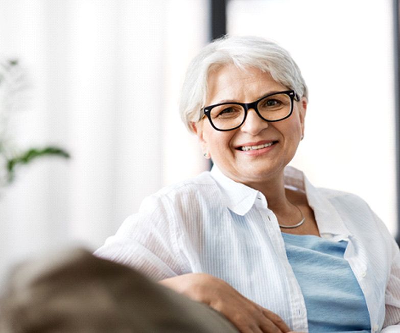 Older woman on couch smiling with implant retained dentures in Jacksonville, FL