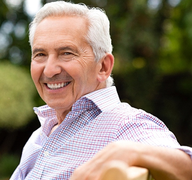 Older man in patterned shirt leaning on bench outside