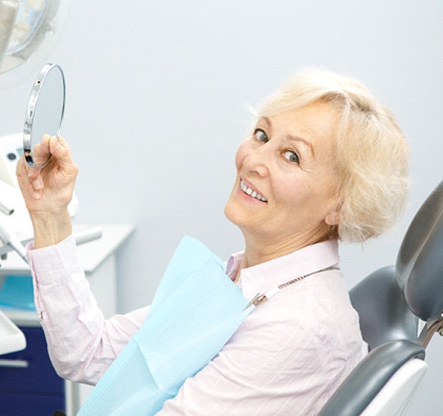 Grinning older woman in dental chair with mirror