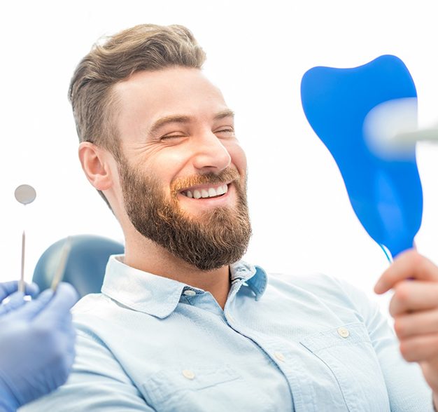 Man with cosmetic dental bonding smiling in dentist's mirror