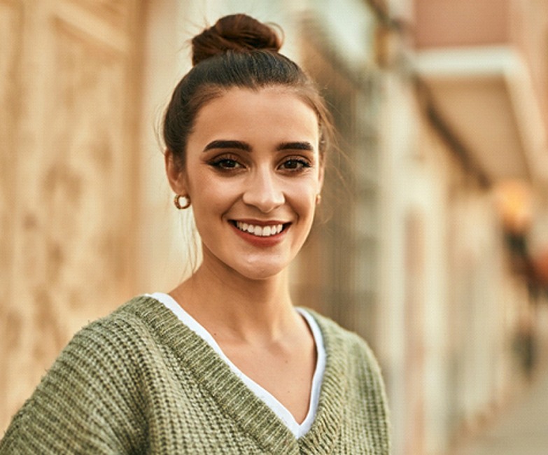 A young woman wearing a green sweater and standing outside after receiving same-day CEREC dental crowns in Bartram Park