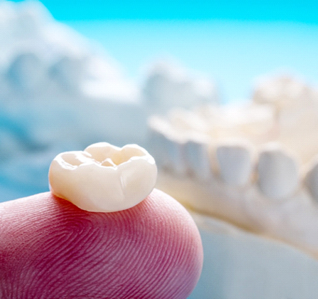 Close-up of finger holding dental crown in Jacksonville, FL