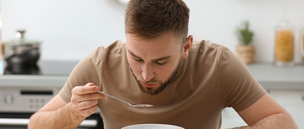 A young man having vegetable soup in the kitchen