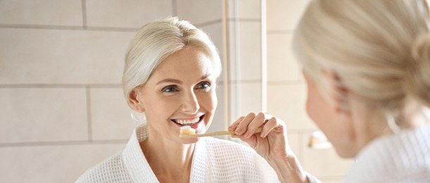 A smiling older woman brushing her teeth in a bathroom
