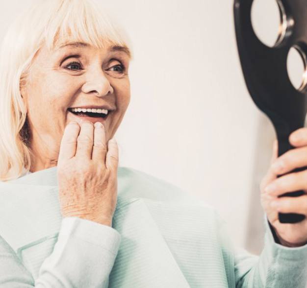 Older woman with dental implants in Jacksonville using a mirror