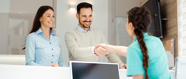 Husband shaking hand of dental employee with wife nearby