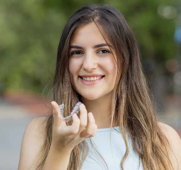 A young female holding an Invisalign clear aligner in preparation for reinserting it into her mouth