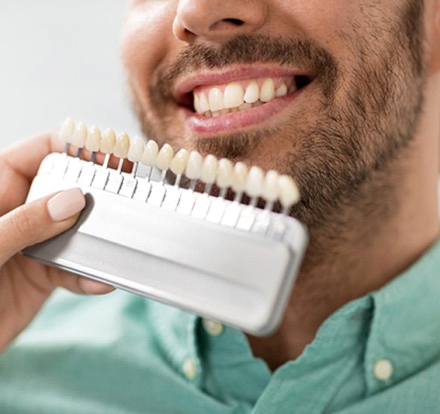 Dentist holding up veneer shades to male patient's smile