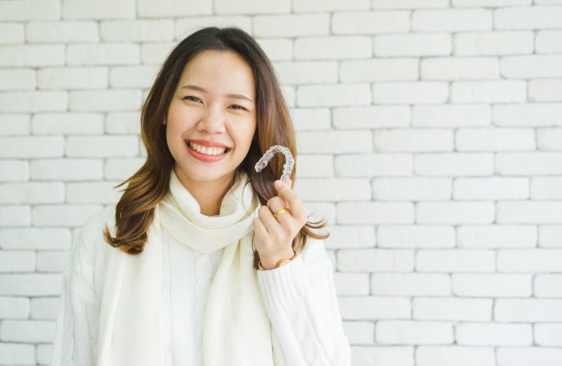 person smiling while holding Invisalign aligner