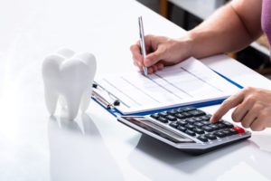 Person calculating costs with a calculator next to a large fake tooth