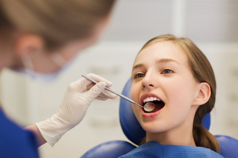 A dentist checking a teen girl’s teeth