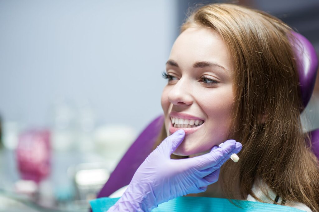 Woman with brown hair in dental chair smiling as dentist touches her chin